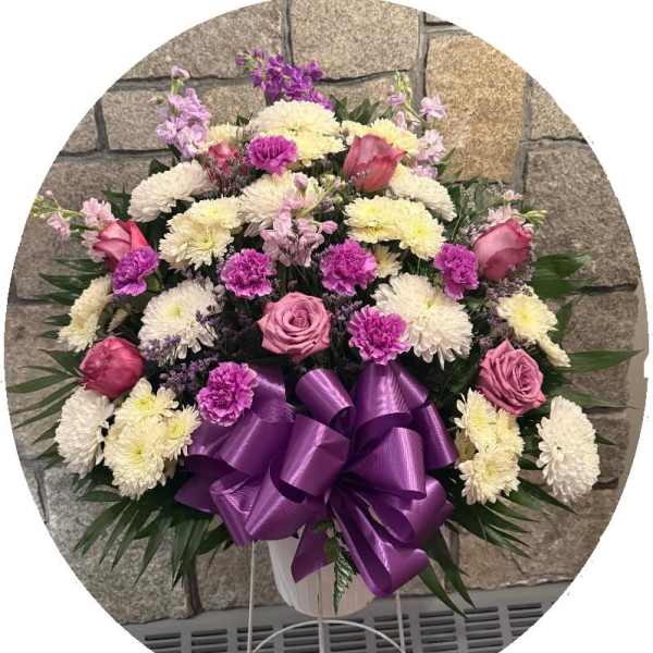 Pink and white floral spray with a purple ribbon bow in a white stand