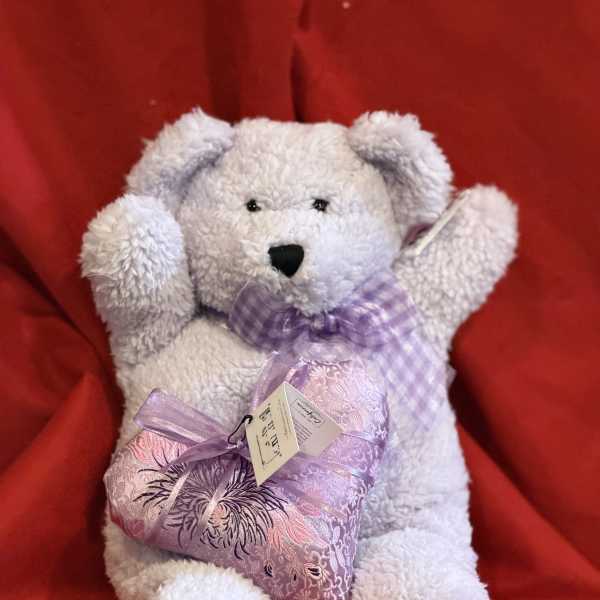 White teddy bear holding a lavender heart pillow on a red background