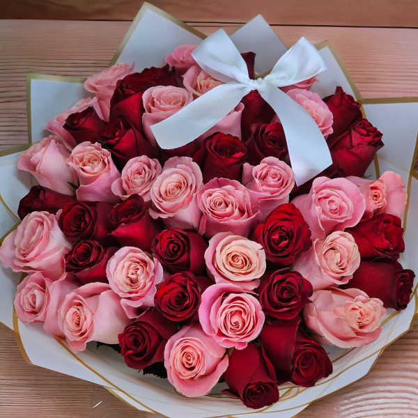 Round bouquet of red and pink roses wrapped in white paper with a white bow