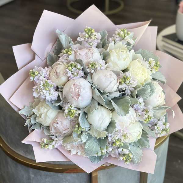 Bouquet of pale peonies and small lavender flowers wrapped in pink paper