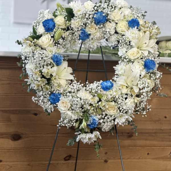 White floral wreath with blue accents on a stand