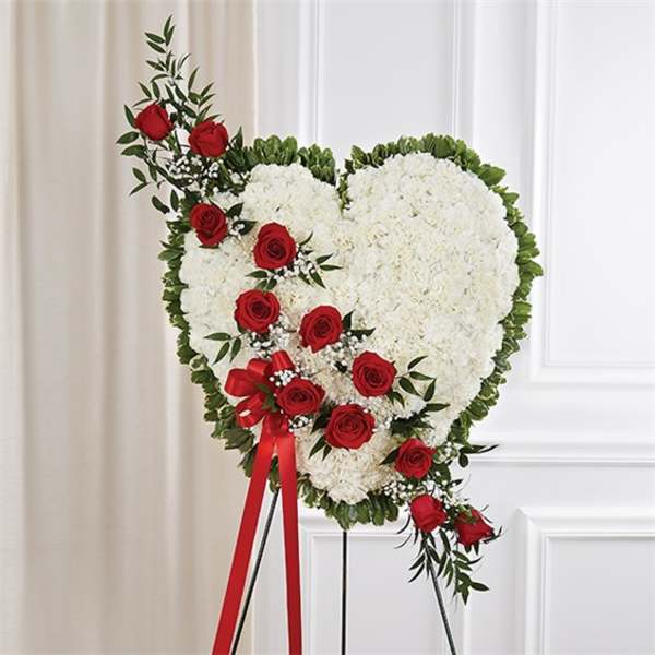 Heart-shaped white floral standing spray with red roses and greenery on an easel.