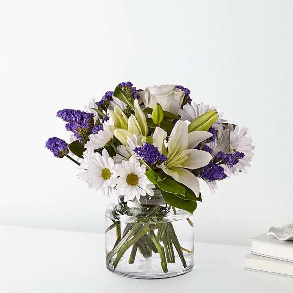 White daisies, lilies, roses, and purple blooms arranged in a clear glass vase.