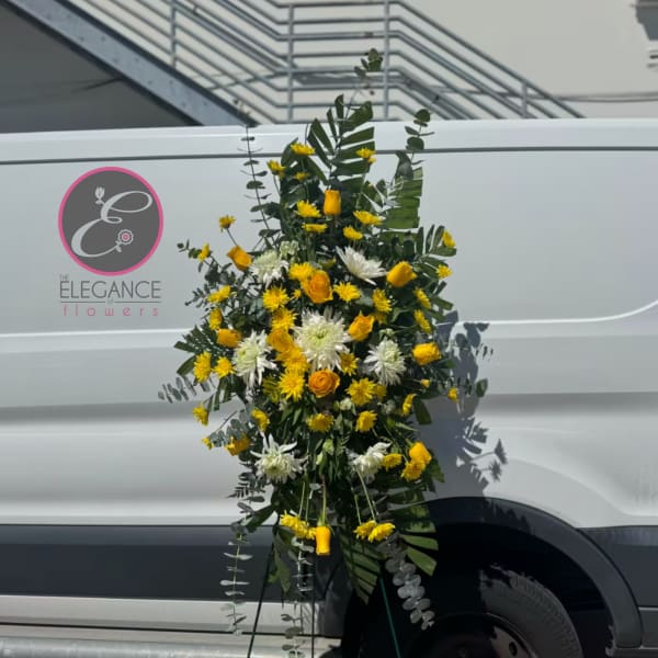 Tall standing floral spray with yellow and white blooms on a metal easel