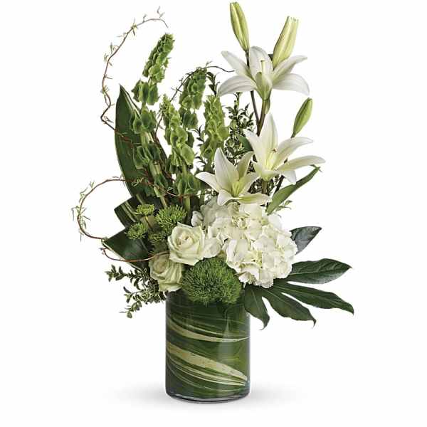 Tall arrangement of white lilies, roses, and hydrangea with green accents in a clear cylinder vase