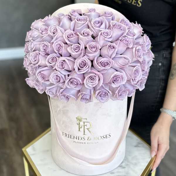 Lavender roses arranged in a round hatbox with a ribbon handle