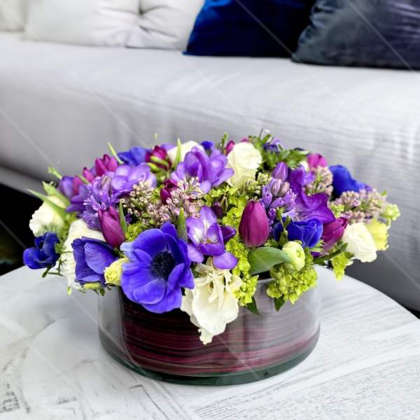 Purple and white floral arrangement in a round glass vase