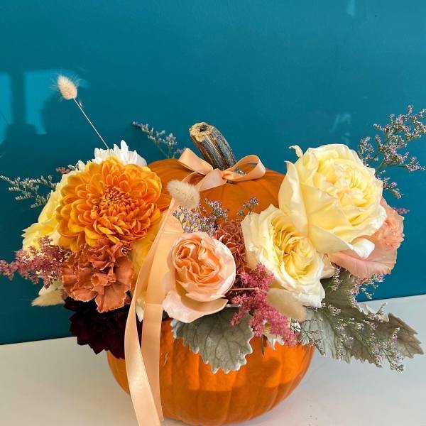 Floral arrangement in a pumpkin with orange, cream, and peach blooms