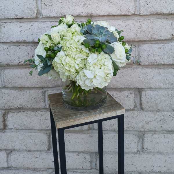 White floral arrangement in a glass vase with green accents