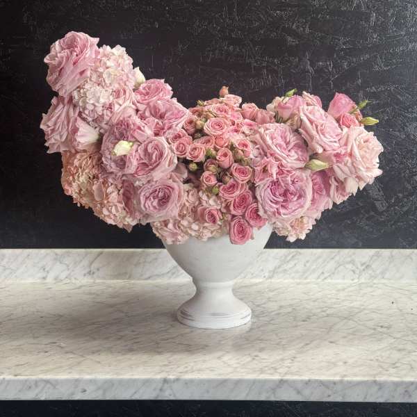 Pink rose arrangement in a white pedestal vase
