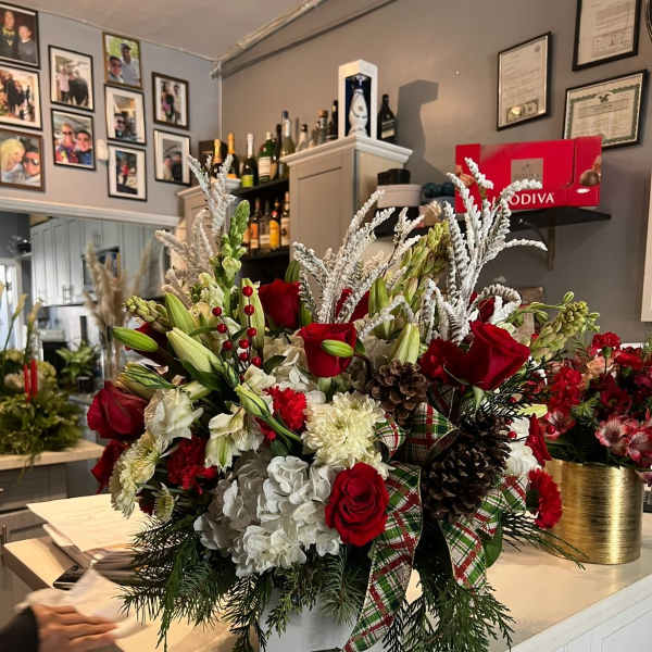 Large holiday floral arrangement with red roses and white blooms in a white container