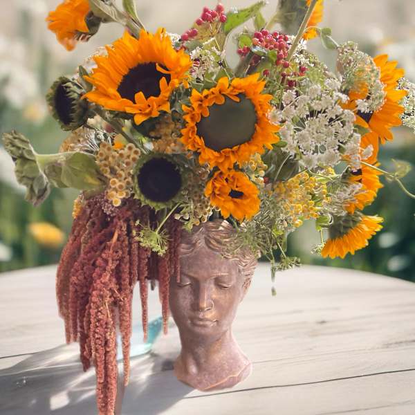 Sunflower arrangement in a sculpted face vase with trailing burgundy amaranthus