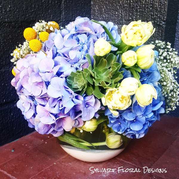Bouquet of blue and lavender hydrangeas with yellow tulips in a bowl vase