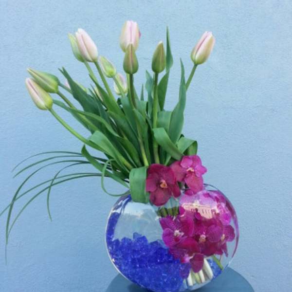 Pink tulips and magenta orchids in a round glass vase