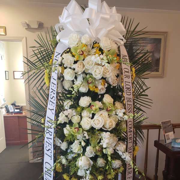 Large white funeral spray with roses and ribbons on a stand