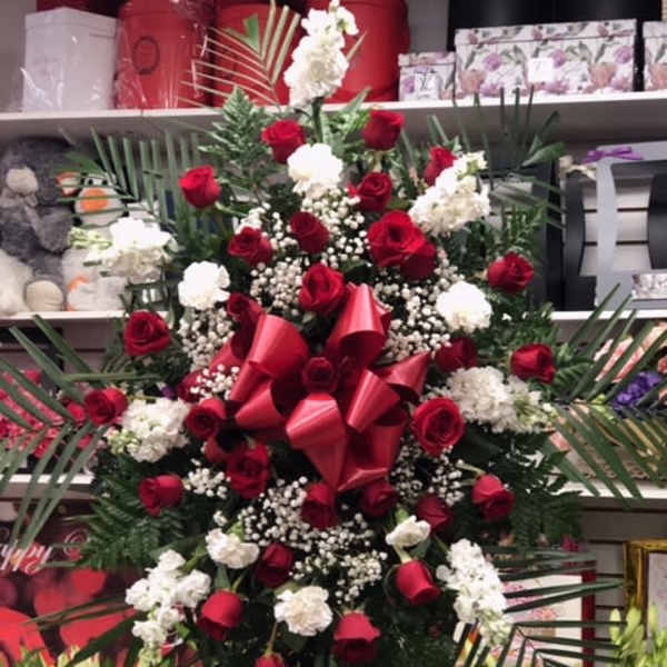 Large standing arrangement of red roses and white carnations with a red bow