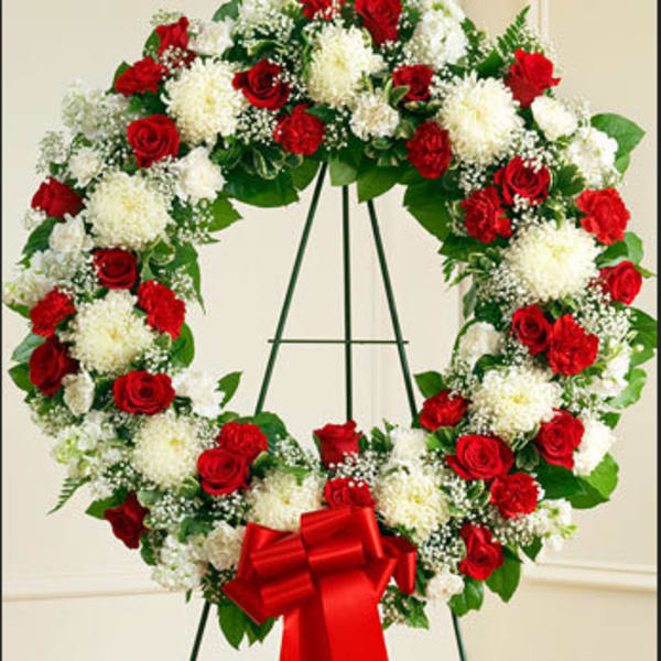 Heart-shaped wreath of red and white flowers on a stand with a red bow