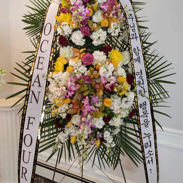 Tall standing floral wreath with white ribbons and mixed blooms
