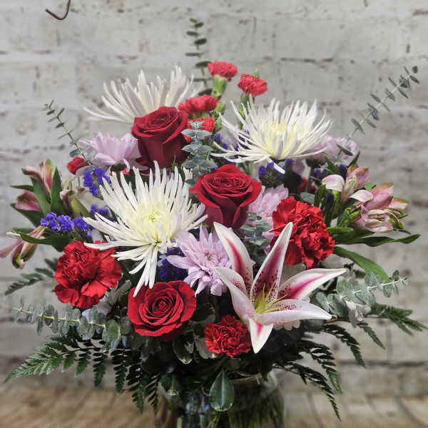 Mixed bouquet with red roses, white lilies, and pink flowers in a glass vase
