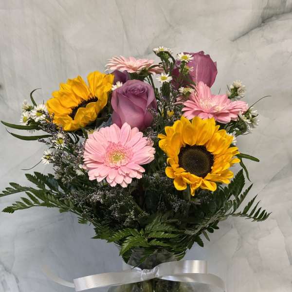 Mixed bouquet with sunflowers, pink gerberas, and a purple rose in a glass vase