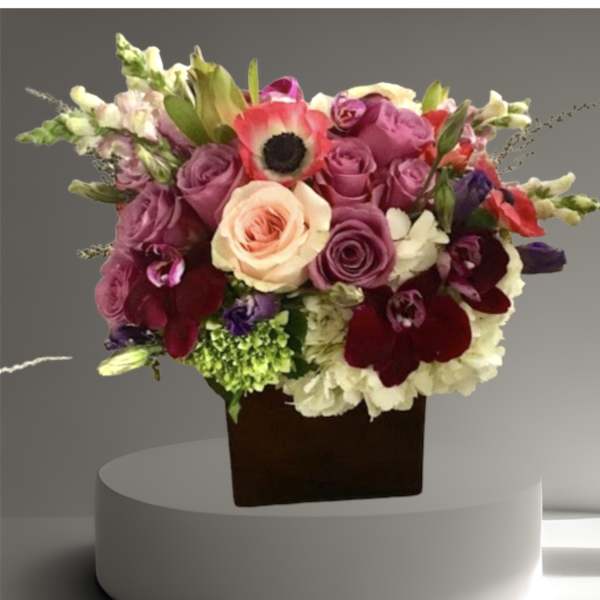 Mixed bouquet of roses, orchids, and snapdragons in a dark square vase