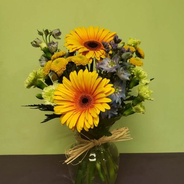 Bouquet of yellow gerbera daisies and mixed blooms in a glass vase