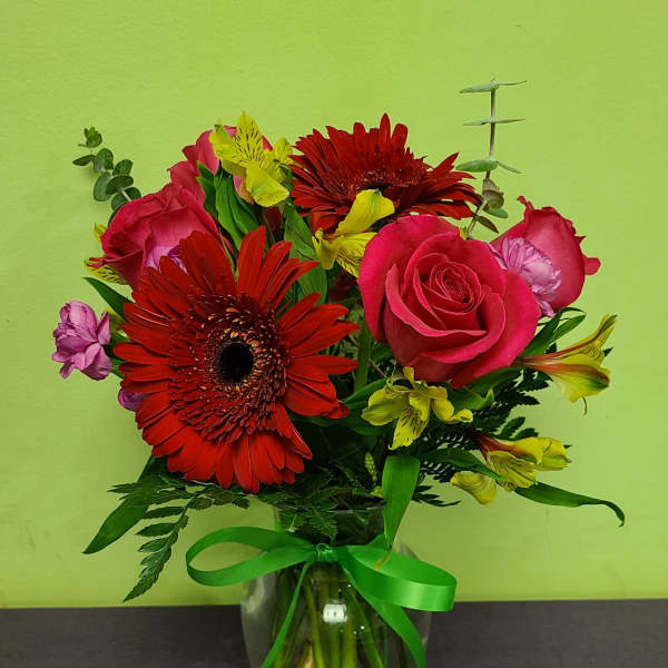 Bouquet of red gerbera daisies, pink roses, and yellow alstroemeria in a glass vase