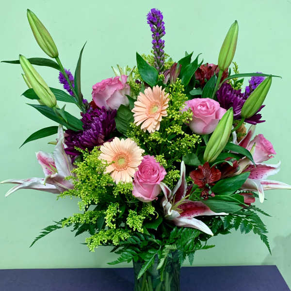 Mixed bouquet of pink roses, lilies, and purple flowers in a glass vase