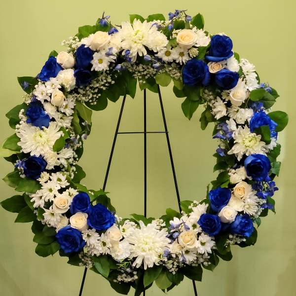 Heart-shaped floral wreath with blue and white flowers on a black stand