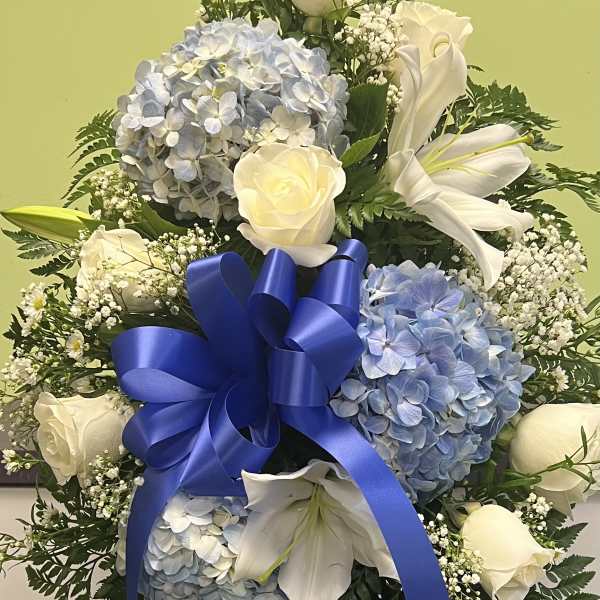 Blue and white floral standing spray with roses, hydrangeas, lilies, and a ribbon bow
