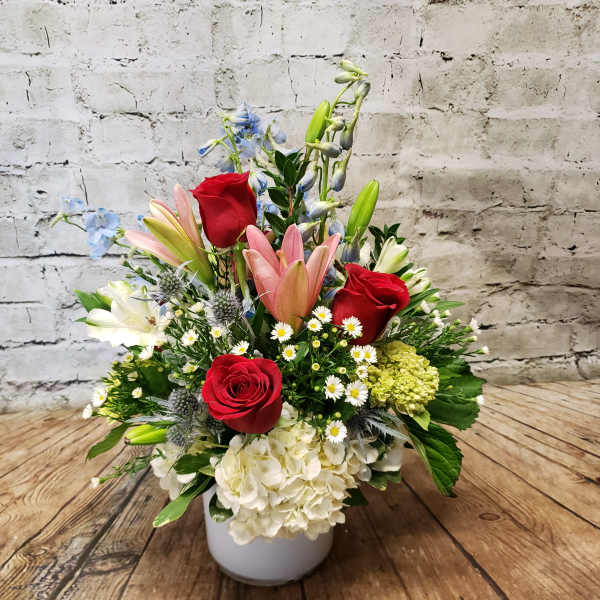 Mixed bouquet in a white vase with red roses, pink lilies, and white hydrangea