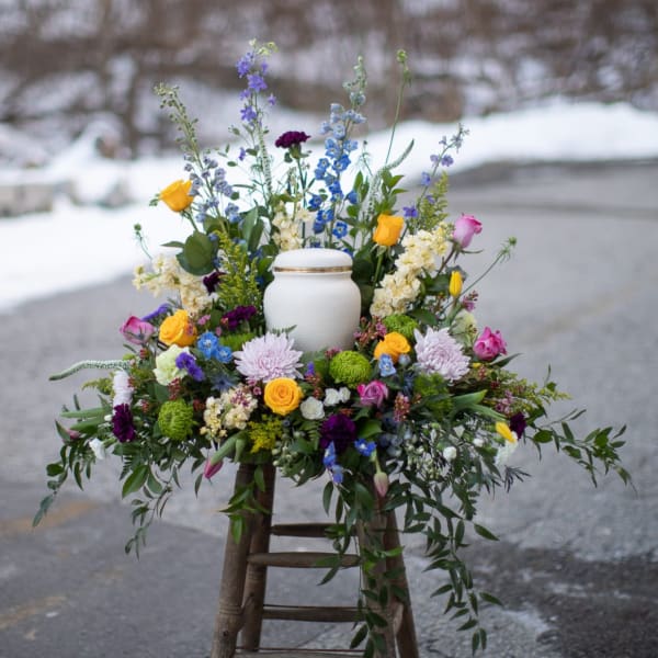 Colorful floral arrangement around a white urn on a stool