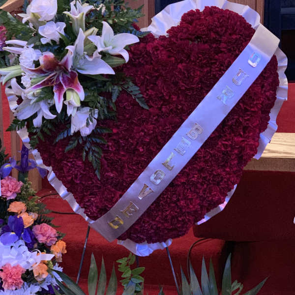 Heart-shaped red floral tribute with white lilies and a ribbon