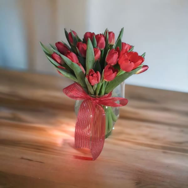 Red tulip bouquet in a clear glass vase with a red ribbon
