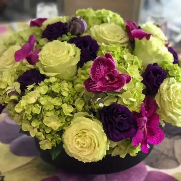 Round bouquet of pale green and purple flowers in a black container