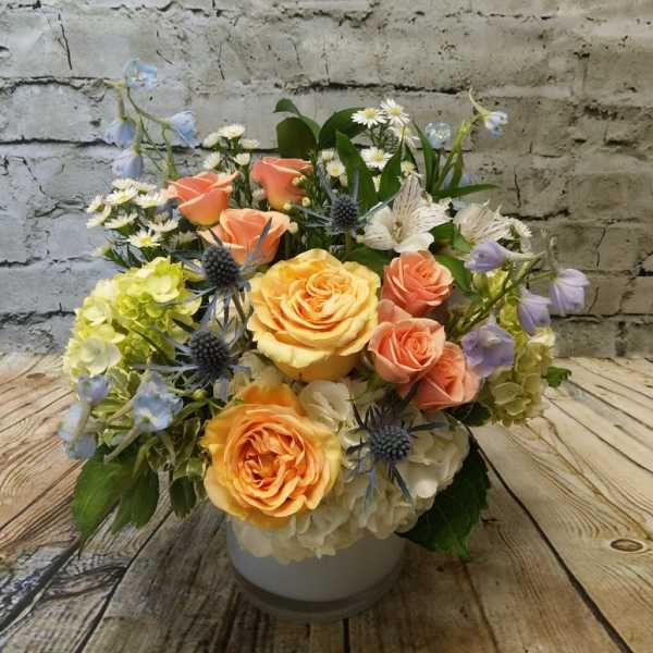 Mixed bouquet of peach roses, hydrangeas, and blue thistle in a white vase