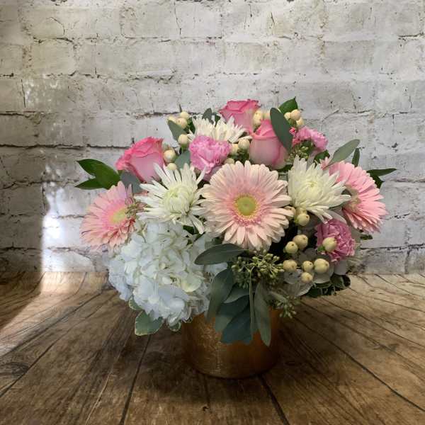 Pink roses and gerbera daisies in a gold vase with white hydrangea