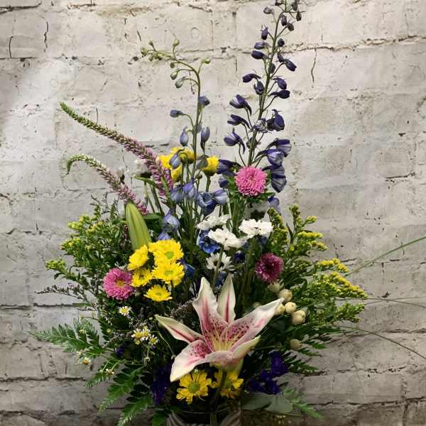 Tall mixed flower arrangement in a glass vase with a striped ribbon
