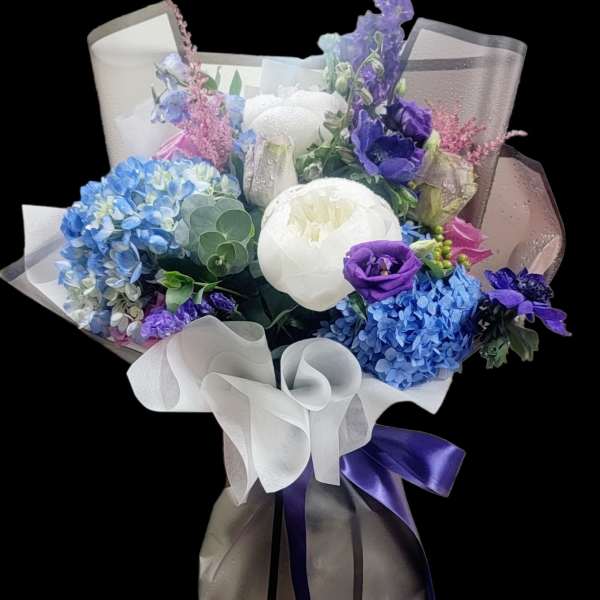 Bouquet of blue, purple, and white flowers wrapped in sheer paper