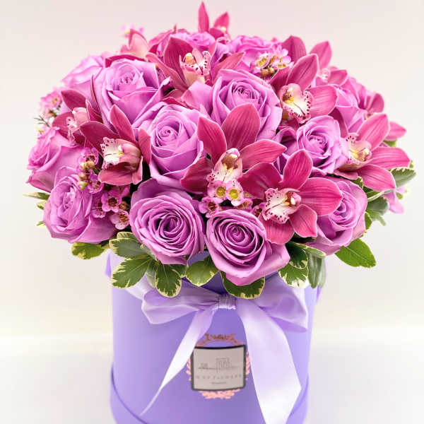 Pink roses and orchids arranged in a lavender hat box with a ribbon