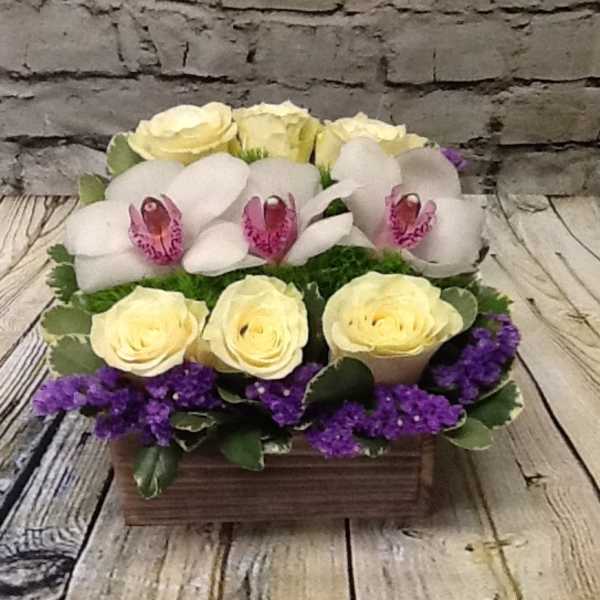 Arrangement of pale yellow roses, white orchids, and purple filler in a wooden box