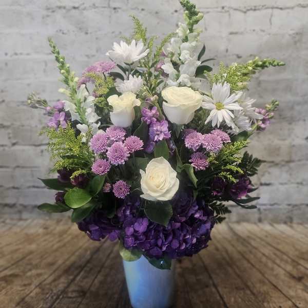 Mixed bouquet in a blue vase with white roses, purple hydrangea, and daisies