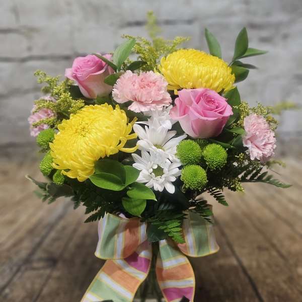 Pink roses and yellow chrysanthemums in a glass vase with a striped ribbon