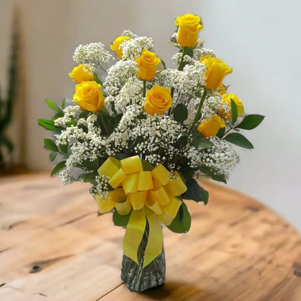 Yellow roses with white baby's breath in a glass vase tied with a yellow ribbon.
