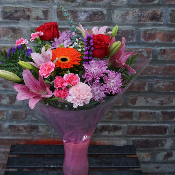 Mixed bouquet of pink, red, and orange flowers wrapped in purple paper