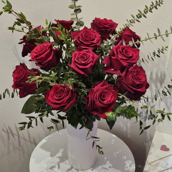 Bouquet of deep red roses in a white vase with airy greenery