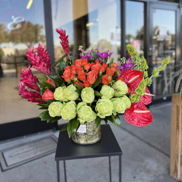 Bright mixed bouquet with roses, anthuriums, and tropical blooms in a gold vase