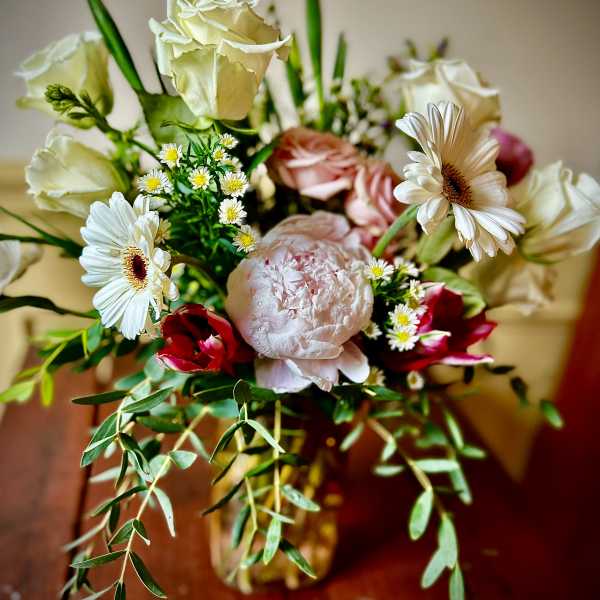 Mixed bouquet of white roses, gerbera daisies, pink peony, and red blooms in a glass vase
