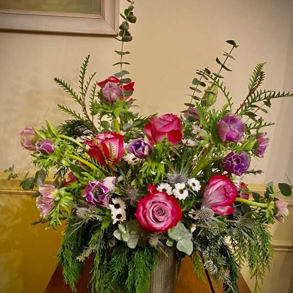 Garden-style arrangement of pink roses and purple anemones in a tall metal vase