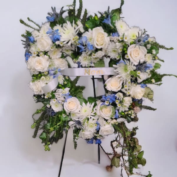 Heart-shaped floral wreath with white roses and blue flowers on a stand